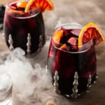 red halloween sangria with apples, oranges, and blackberries with smoke in a skeleton glass